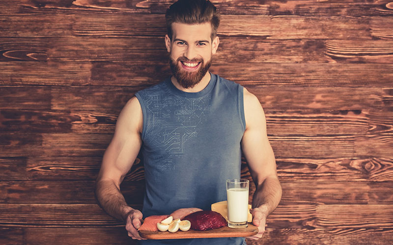 smiling man with muscle gaining foods on a tray
